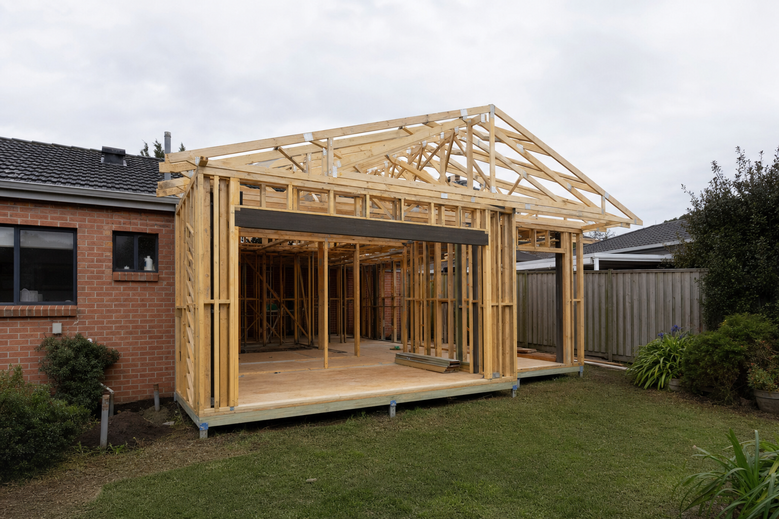 A single-storey rear extension under construction on a suburban Melbourne home, with a timber-framed structure against the existing brick house and a timber boundary fence in the background