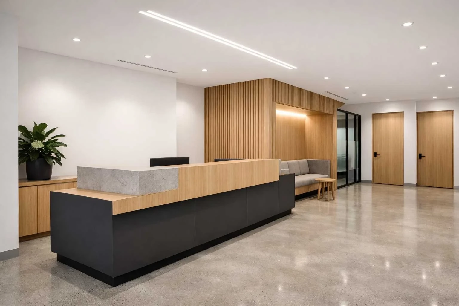 A commercial office reception with a dark reception desk topped in timber and stone, a timber slat feature wall, a grey lounge, and two timber doors