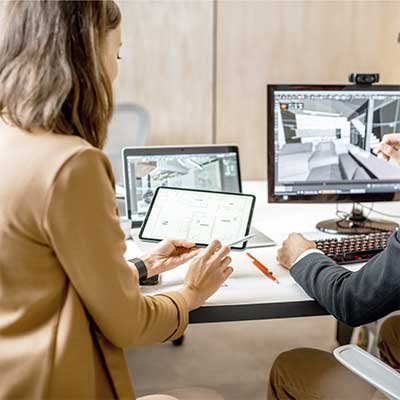 Two people working on a design project at a desk with multiple screens and a tablet.